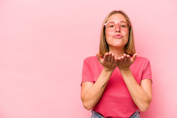 Young caucasian woman isolated on pink background folding lips and holding palms to send air kiss.