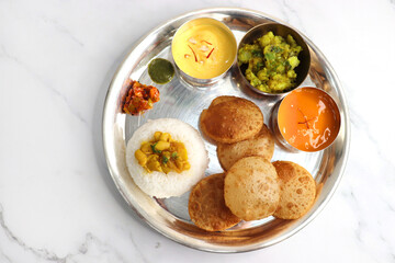 Indian vegetarian Thali or platter includes Aloo ki sabji, dal rice, Puri bhaji, Shrikhand or Srikhand, Aamras, papad, pickle, and chutney. Mashed potato curry or masala. Indian Festival food Thali.