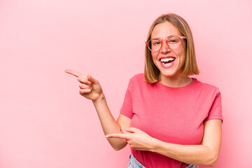 Young caucasian woman isolated on pink background pointing with forefingers to a copy space, expressing excitement and desire.