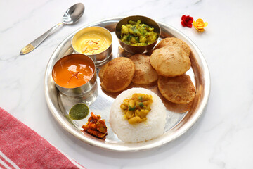 Indian vegetarian Thali or platter includes Aloo ki sabji, dal rice, Puri bhaji, Shrikhand or Srikhand, Aamras, papad, pickle, and chutney. Mashed potato curry or masala. Indian Festival food Thali.