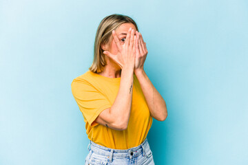 Young caucasian woman isolated on blue background blink through fingers frightened and nervous.