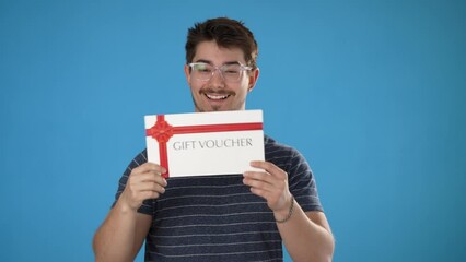 Portrait of smiling happy handsome young man striped t-shirt holding gift certificate voucher coupon isolated on blue background in studio.