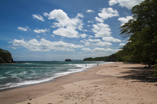 Scenic View Of A Beach And Two People In The Distance Walking With The Blue Sky In The Horizon