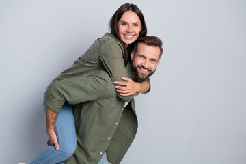 Portrait of attractive cheerful amorous couple married spouses piggy backing isolated over grey...
