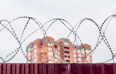 Barbed wire on fence with modern residential building on background. Protection and prohibition concept.
