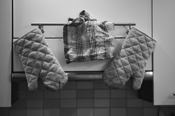 Grayscale shot of two oven mitts and a towel hanging on a kitchen rack