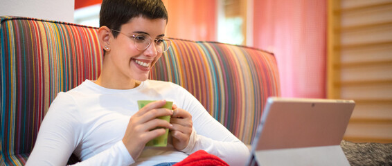 Young woman drinking coffee and using laptop while lying on the couch at home