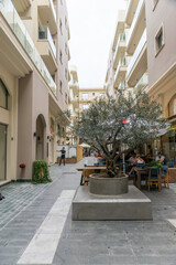 Narrow alley with a cafe on the side of the road and a tree in the middle of the road on Cyprus - obrazy, fototapety, plakaty