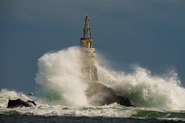 Old rusty lighthouse in the Black Sea with giant waves crashing on it in Ahtopol, Bulgaria