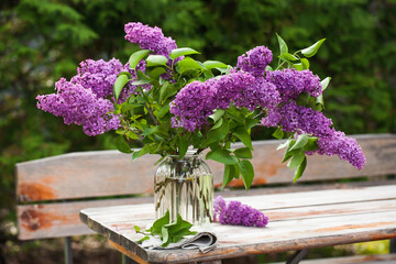 Beautiful bouquet of lilacs in a vase on a wooden table in nature.