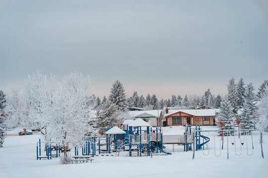 Snow-covered playground during winter with snowy trees and small houses in the background