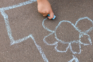A child draws on the sidewalk with blue chalk. Hobby for children outdoors.