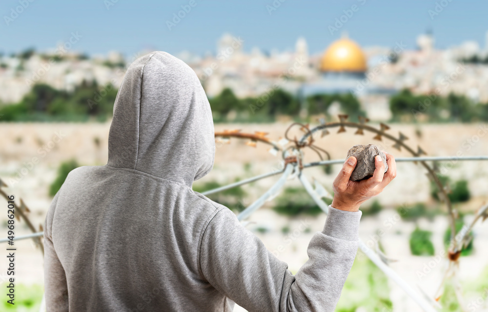 Wall mural Rear view of a hooded person throwing stones at a metal balla in jerusalem