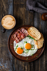 Fried eggs with bacon and herbs, 2 white bread toasts. On the table is a napkin, spices, a glass of champagne. Dark brown wooden background. Breakfast menu for cafe, restaurant, bar.