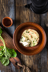 Plate of couscous with tomatoes, vegetables and feta cheese. Basil leaves, tomatoes, herbs and teapot with cup are on a wooden table. Menu for restaurant, cafe, bar. Top view.