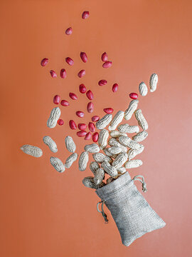 Vertical shot of peanuts and red seeds coming out of a fabric sac on an orange background