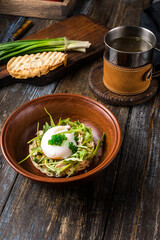 Chicken soup with arugula, chicken, poached egg in a deep bowl. On a wooden table are toasted bread, fresh onions, a mug of broth. For the restaurant menu. Close up.