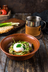 Chicken soup with arugula, chicken, poached egg in a deep bowl. On a wooden table are toasted bread, fresh onions, a mug of broth. For the restaurant menu. Close up.