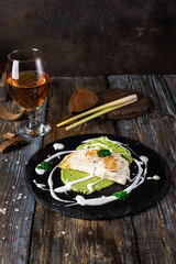 On a round serving board mashed broccoli and vegetables, grilled fish fillet with white cream...