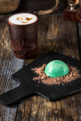 On the serving board is a gourmet dessert green hemisphere with chocolate chips. On a wooden table...