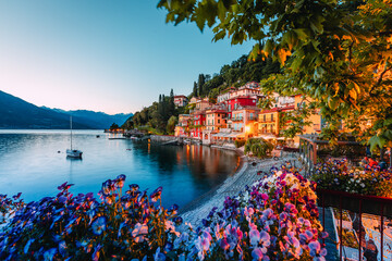 Village of Varenna on Lake Como at sunset with illuminated houses and colorful flowers in the foreground