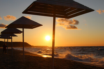 Silhouettes of wooden beach umbrellas on wet sand in stormy weather at summer sunset 