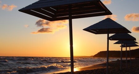Silhouettes of wooden beach umbrellas on wet sand in stormy weather at summer sunset 