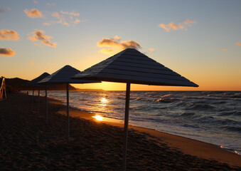 Silhouettes of wooden beach umbrellas on wet sand in stormy weather at summer sunset 