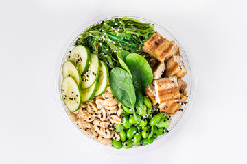 Poke bowl with rice, tofu, edamame beans, cucumber, chukka, spinach and peanuts on a white background.  Plastic tableware for delivery. Top view.