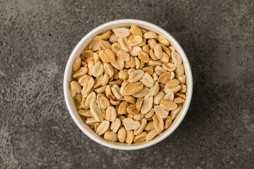 peeled peanuts in a round bowl on a gray textured background. Top view.