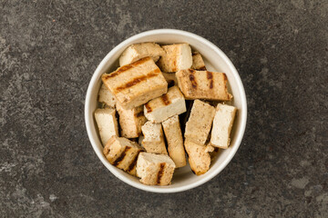 Grilled pieces of tofu cheese in a round bowl on a gray textured background. Top view.