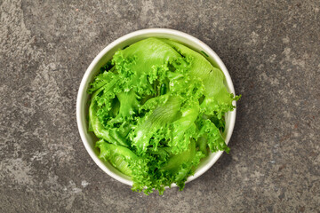 A bowl of frillis lettuce leaves on  gray textured background. Top view.
