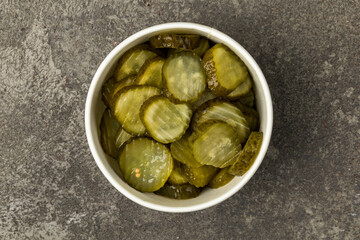 A bowl of marinated cucumbers on a gray textured background. Top view.