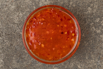 A cup with sweet chili sauce. Gray textured  background. Top view.