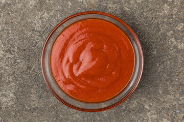 A cup with ketchup sauce. Gray rextured background. Top view.