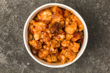 A bowl of chicken marinated in sweet chili sauce. On a gray textured background. Top view.