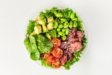Poke bowl with tuna, salad leafs, edamame beans, avocado, cherry tomatoes and spinach on awhite...