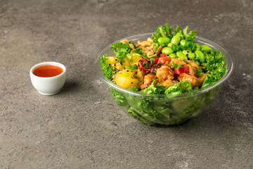 Poke bowl with chicken in a sweet sauce, salad leafs, edamame beans, parsley, pineapple and peanuts on a gray textured background. Sweet chili sauce and pineapple slices.  Copy space. Close up.