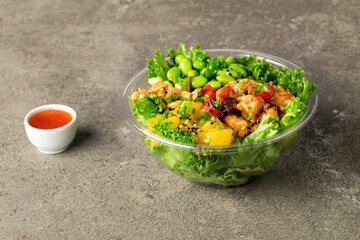 Poke bowl with chicken in a sweet sauce, salad leafs, edamame beans, parsley, pineapple and peanuts on a gray textured background. Sweet chili sauce and pineapple slices. Copy space. Close up