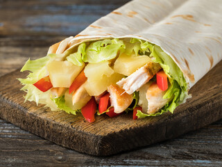 Chiken pineapple shawarma in lavash with bell and lettuce leaves. On a wooden brown background. Close up.