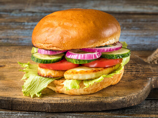 Chicken burger with tomatoes, onions, cucumbers. On the cutting board. Brown wooden background. Close up.