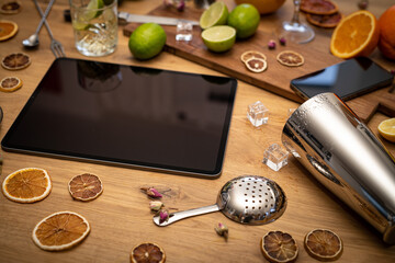 Online cocktail course with blank tablet, smartphone and bartender tools on wood kitchen table
