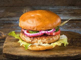 Hamburger with tomatoes, onions, cucumbers. On the cutting board. Brown wooden background. Close up.