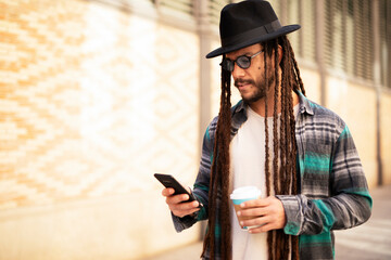Handsome guy drinking coffee while walking in the street. Modern fashion man using the phone..