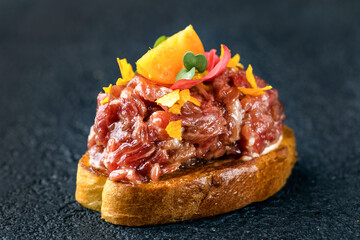 Tapas with beef tartare with sauce, spices and physalis. Dark gray textured background. Close up.