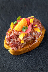 Tapas with beef tartare with sauce, spices and physalis. Dark gray textured background. Close up.