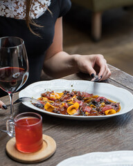 The girl at the table in the restaurant is eating beef carpaccio with a knife and fork. Serving for...