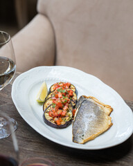 On the table in the restaurant is an oval dish with grilled fish with grilled eggplant cut into slices and vegetables. Close up