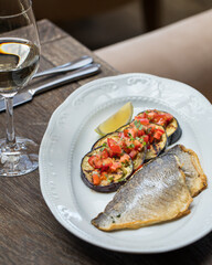 On the table in the restaurant is an oval dish with grilled fish with grilled eggplant cut into slices and vegetables. Close up
