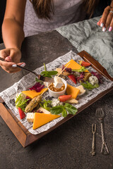 The girl dips a piece of brie cheese into a sauce made of honey and pine nuts. On the table is a plate with hard and soft cheeses, berries and nuts. Close up